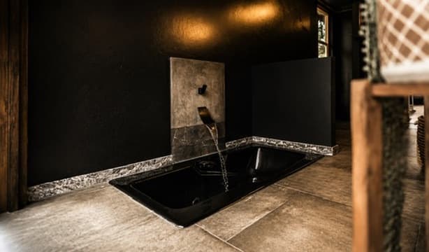 Sunken black bath with sculptural wall-mounted faucet